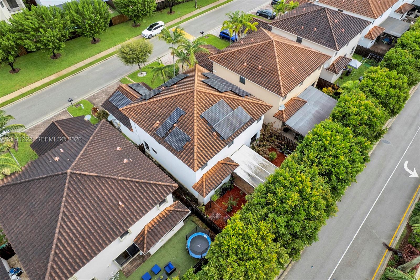 Aerial perspective featuring a multi-story residence with a clay tile roof, integrated solar panel system, and rear hardscaping