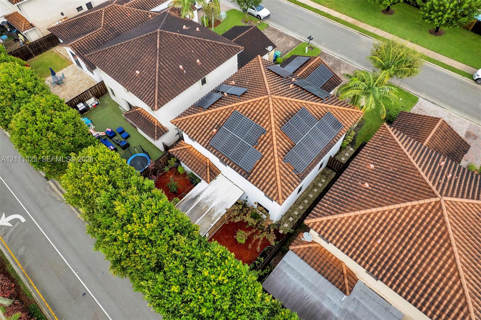 Multi-level residence featuring a clay tile roof, roof-mounted solar energy panels, white stucco exterior, and a partially covered rear patio