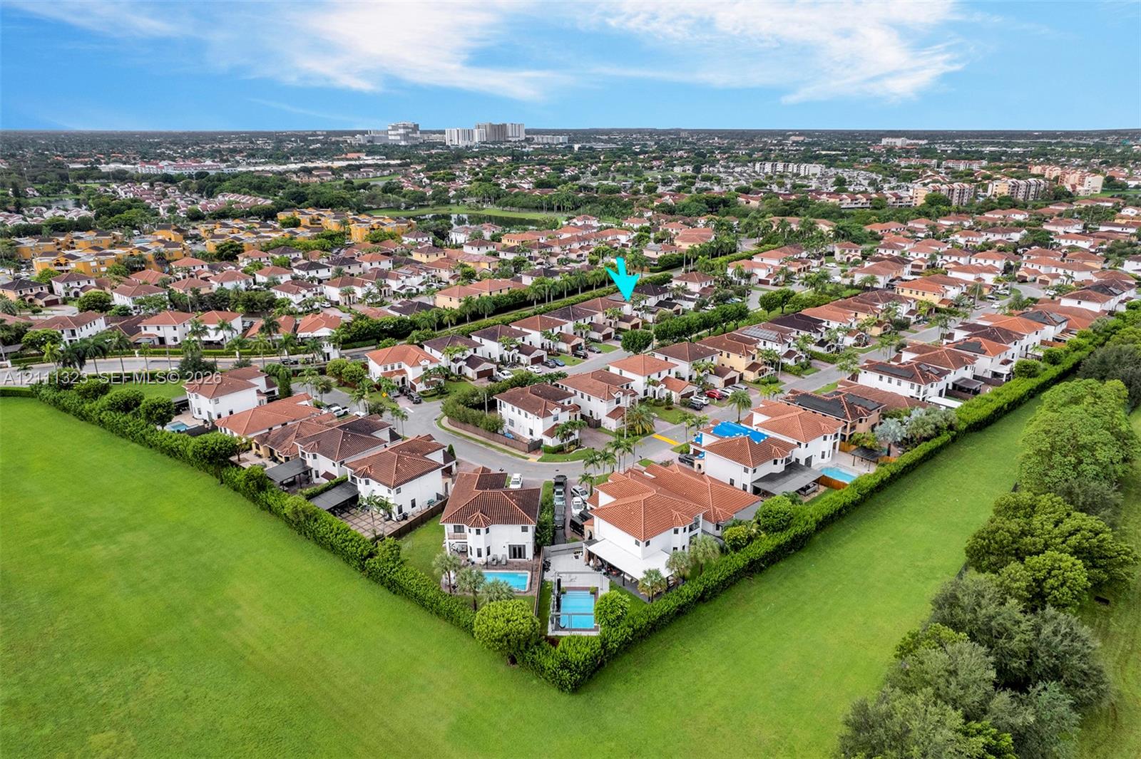 Aerial perspective of a suburban neighborhood featuring multi-story residences with tiled roofs, interspersed with paved roadways and manicured green spaces