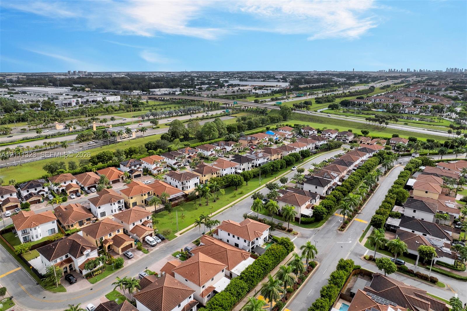 Aerial perspective of a residential community featuring tile roofs, paved roadways, sidewalks, and established landscaping including mature palm trees