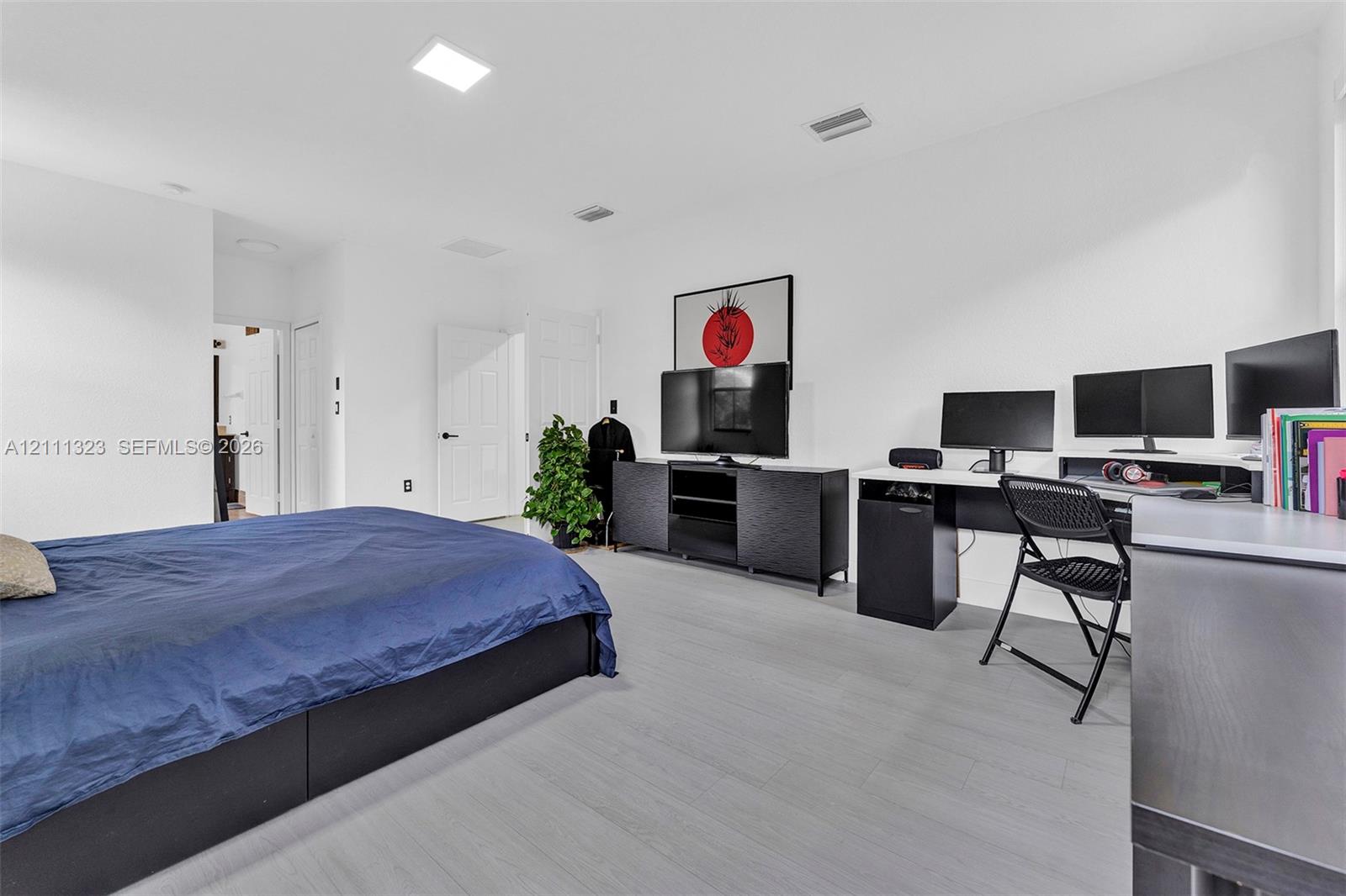 Spacious room featuring light-toned wood-finish flooring, recessed LED lighting, and white interior doors with matte black hardware