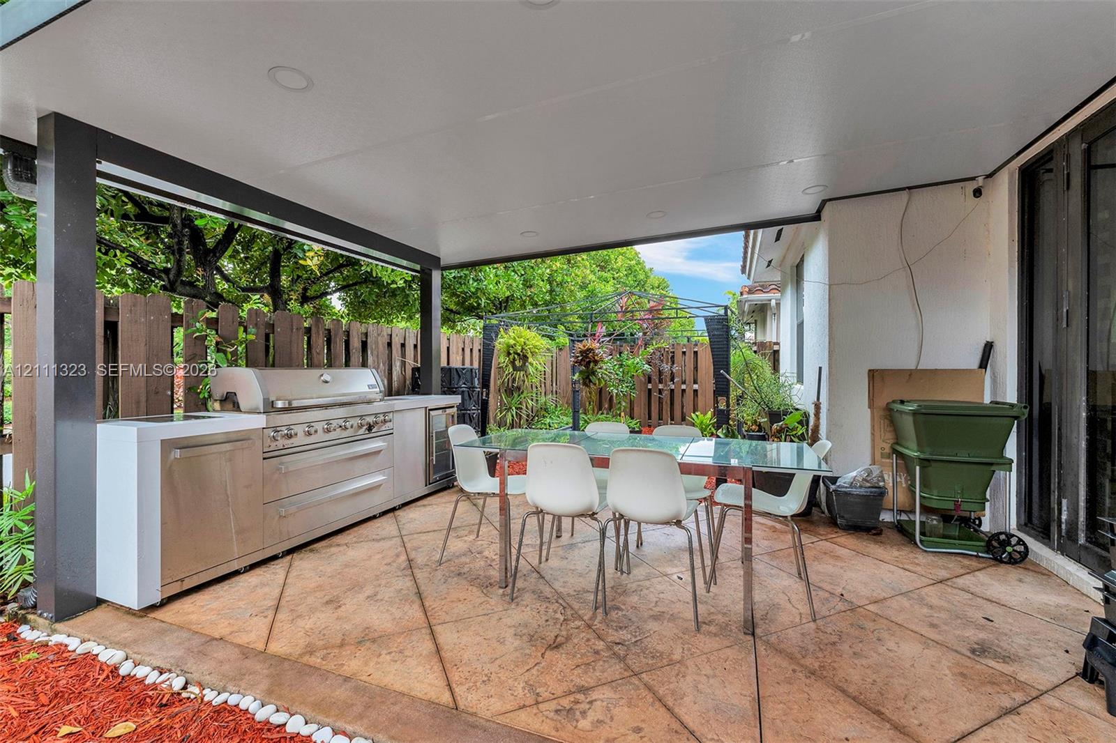 Covered outdoor patio featuring stamped concrete flooring, a built-in stainless steel kitchen module, recessed ceiling lighting, and a fenced perimeter