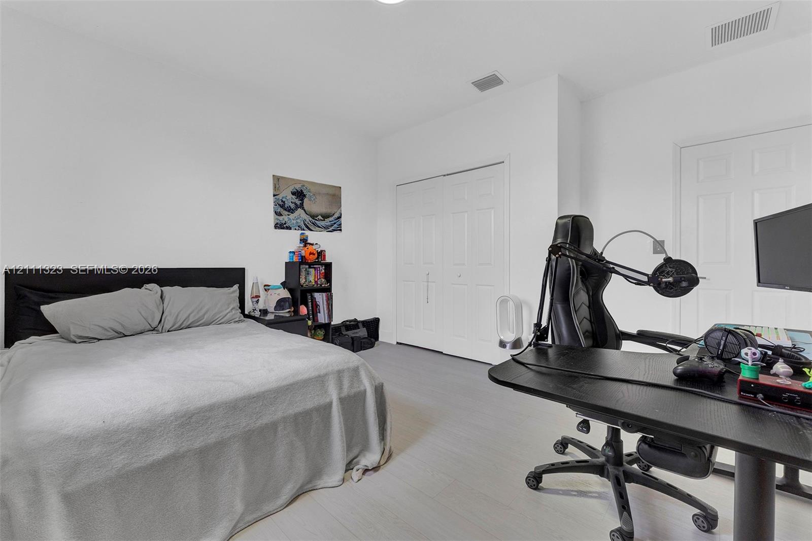 Neutral-toned interior space featuring wood-finish flooring, white walls, and a multi-panel closet with white doors
