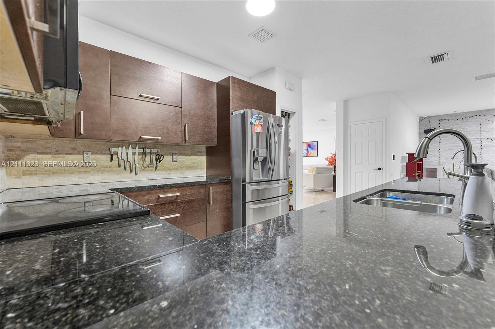 Kitchen featuring dark wood-finish cabinetry, black stone countertops, integrated stainless steel appliances, and a textured tile backsplash
