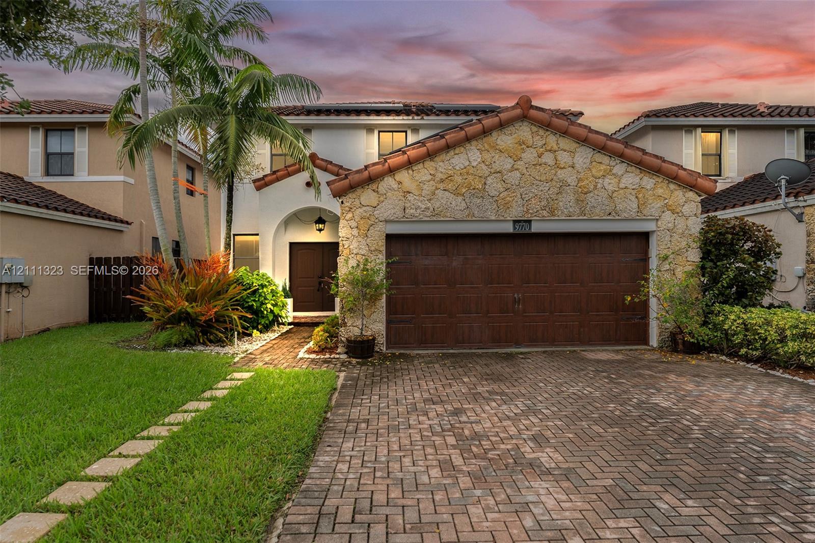 Two-story exterior featuring natural stone veneer, a clay tile roof, and a brick-paver driveway