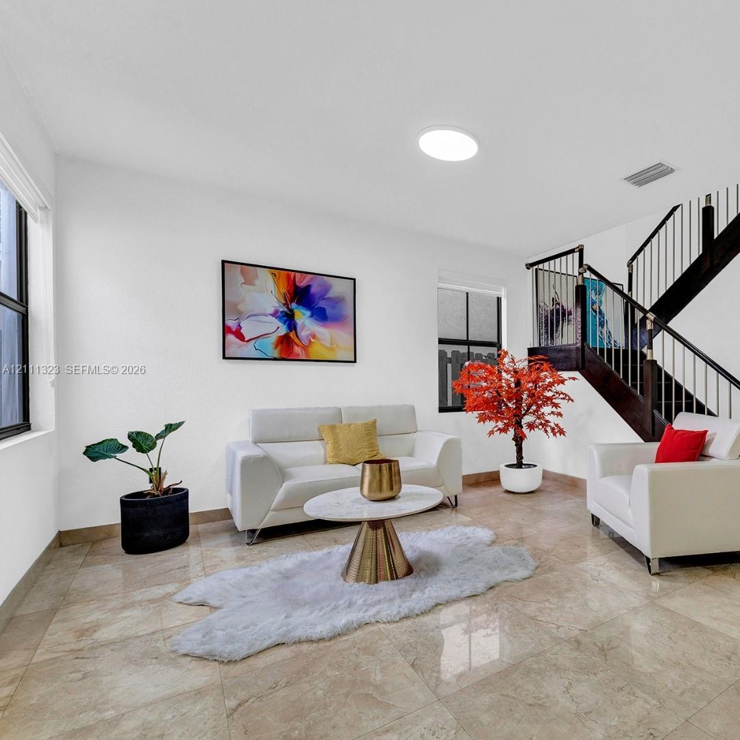 Open living area featuring large-format tile flooring, a dark wood staircase with metal balusters, and windows with white framing