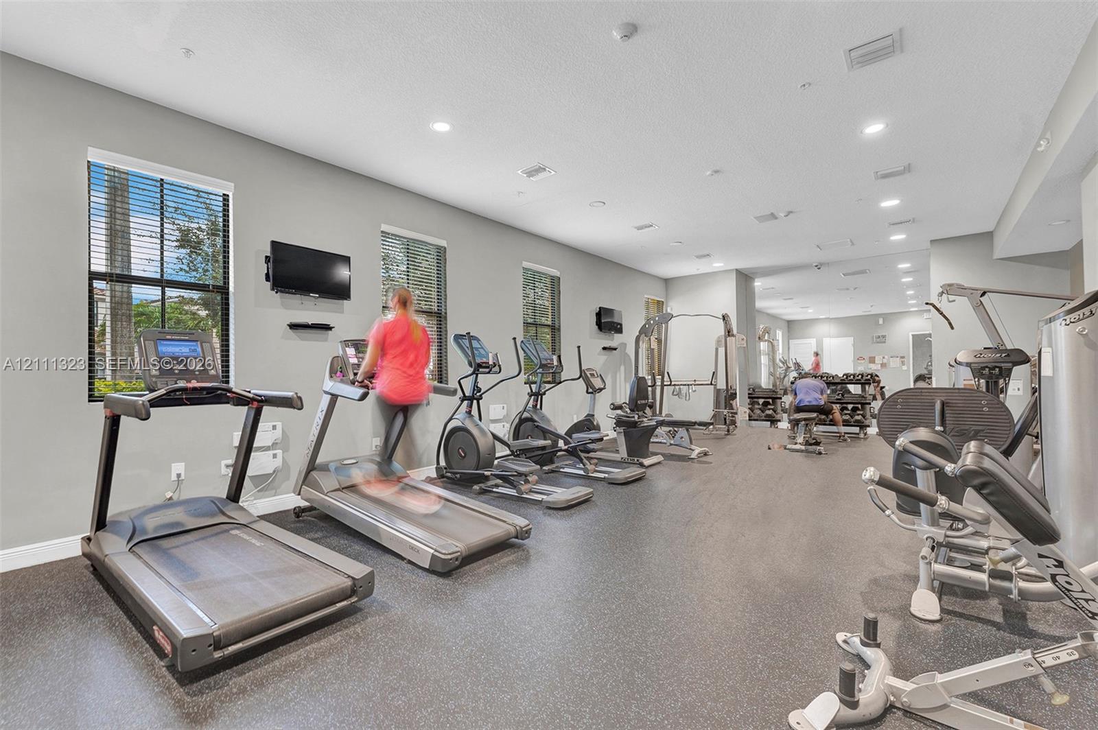 Fitness center featuring rubber flooring, recessed ceiling lighting, and multiple windows with horizontal blinds
