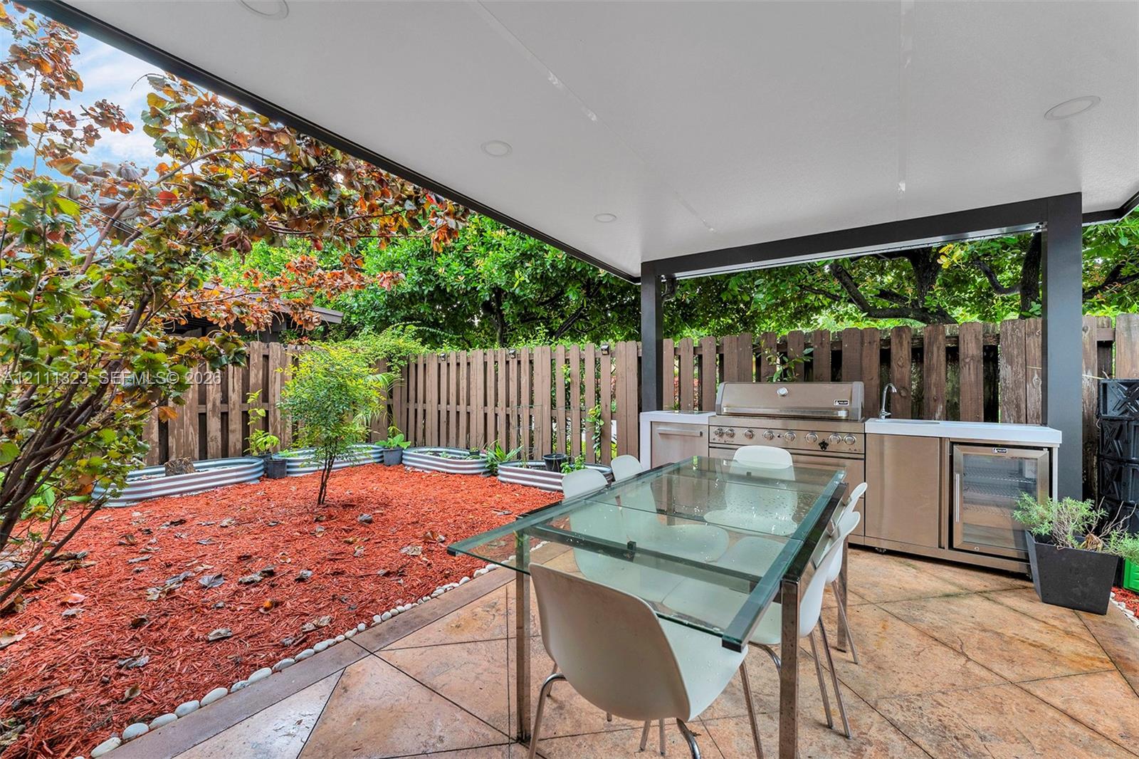 Covered patio featuring stamped concrete flooring, recessed lighting, and a built-in outdoor kitchen with stainless steel appliances, a sink, and a beverage refrigerator, enclosed by a wood privacy fence