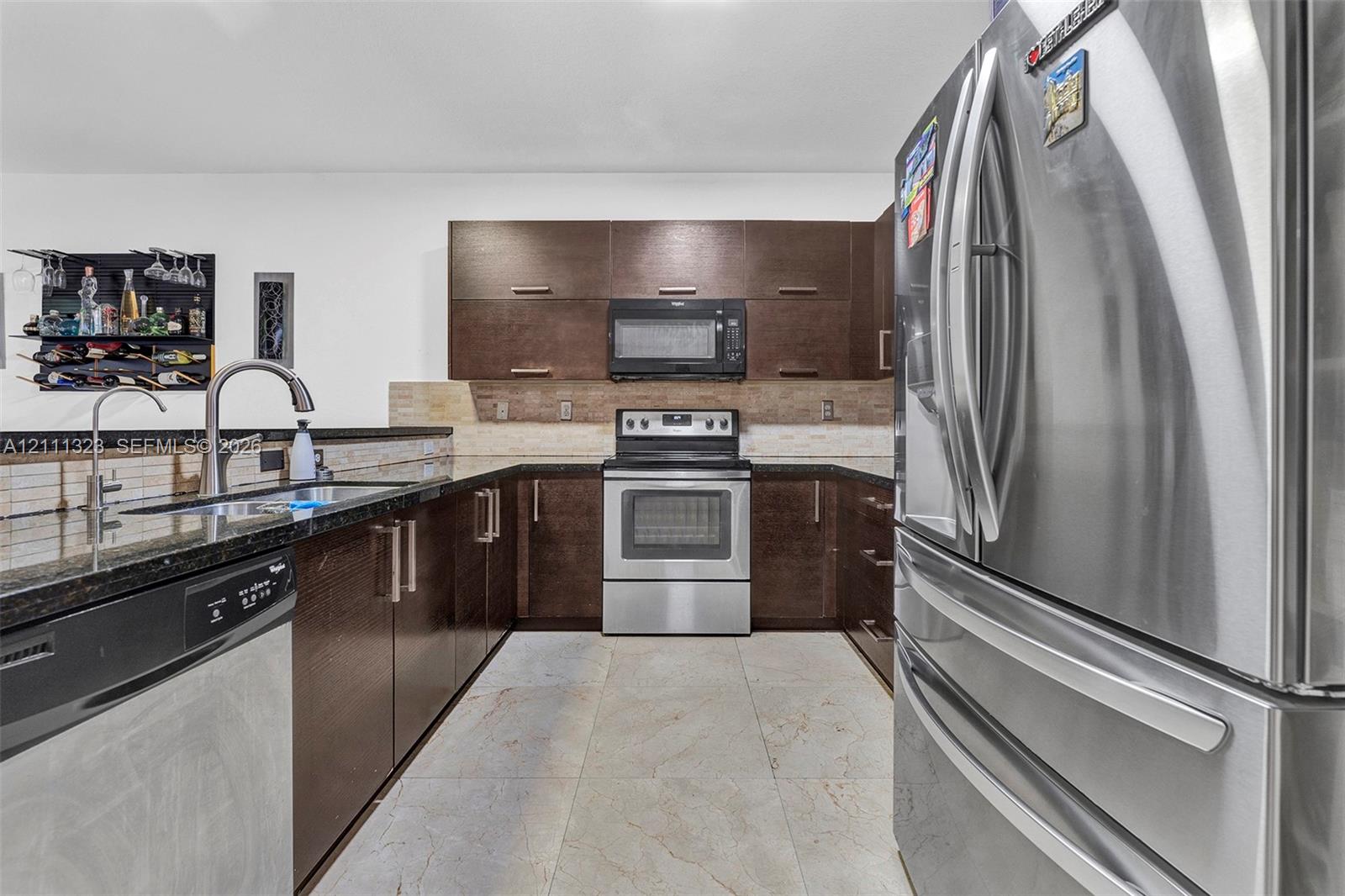 Kitchen featuring dark wood-finish cabinetry, stainless steel appliances, a stone countertop, a tile backsplash, and light-toned tile flooring