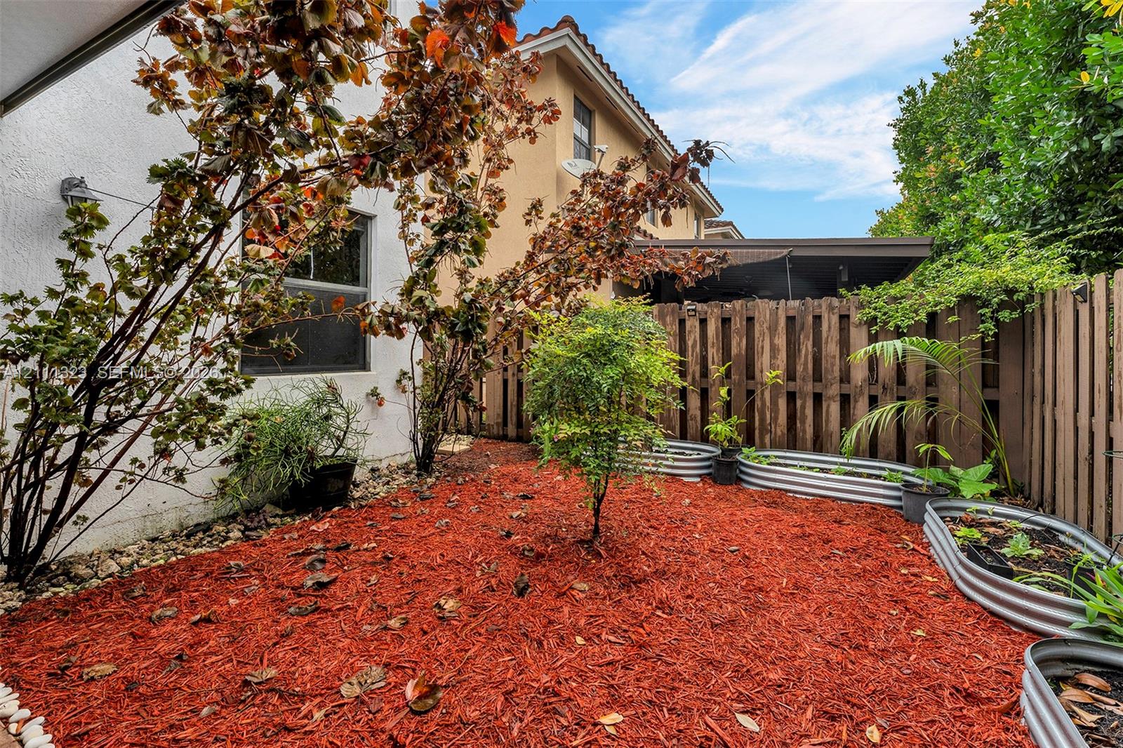 Private outdoor space featuring ground-level garden beds with corrugated metal framing, perimeter wood fencing, and mulch landscaping