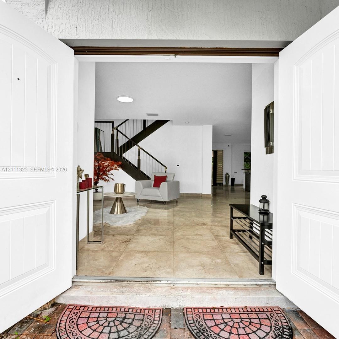 Double entry doors opening to a large-format tile foyer featuring an open-riser staircase with metal railings