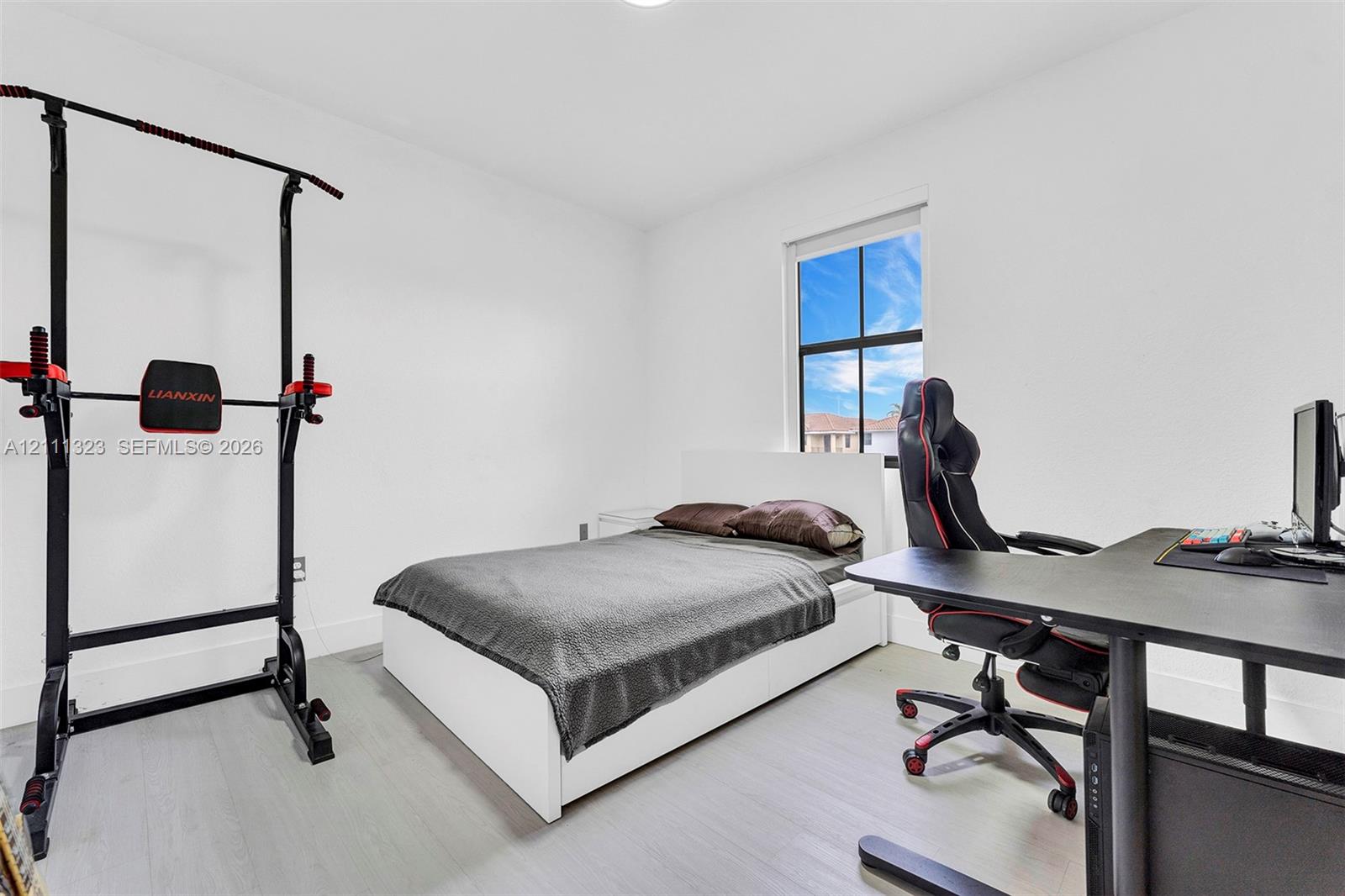 Room featuring wood-finish flooring, crisp white walls, and a window with black muntins