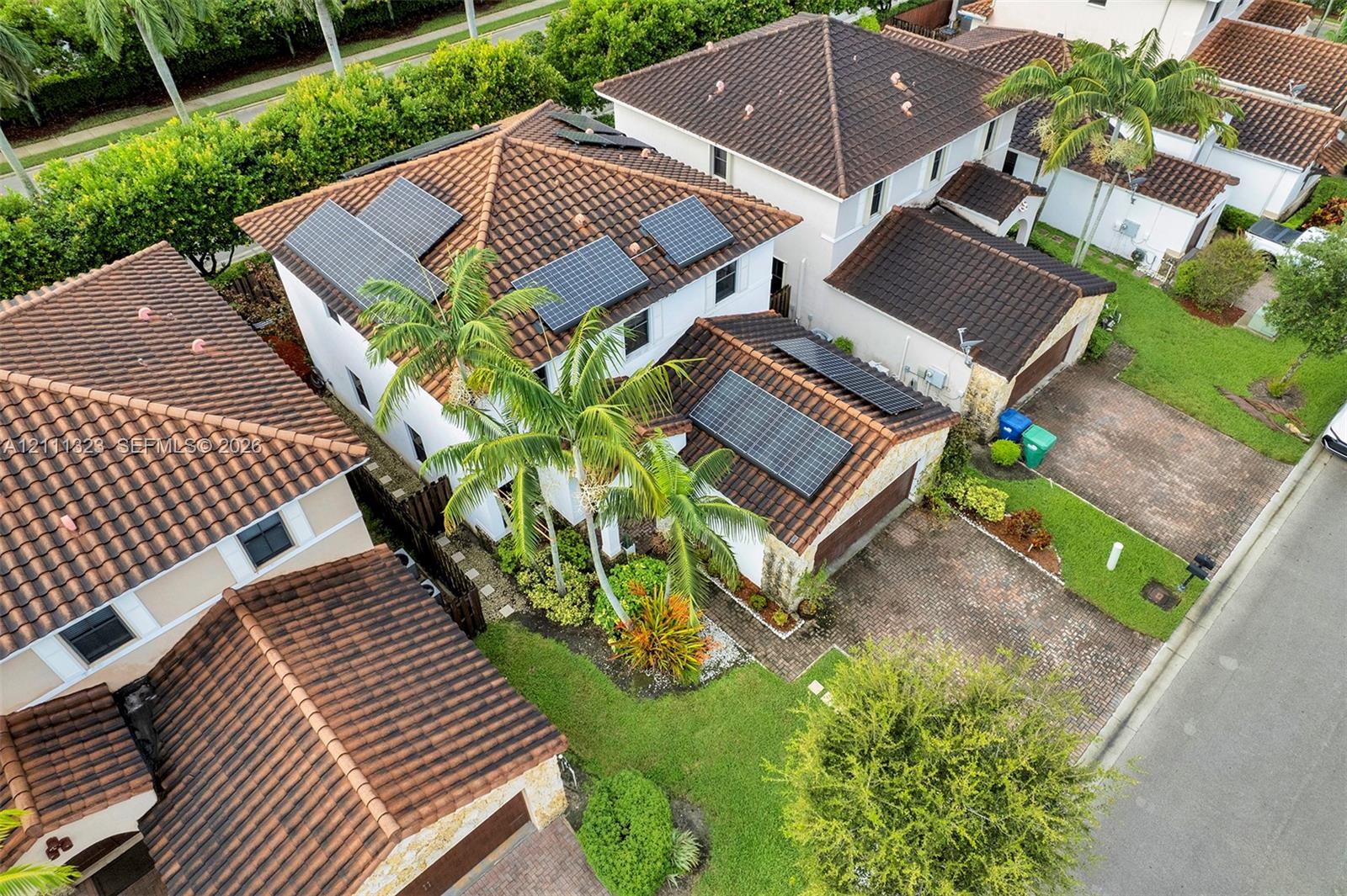 Multi-story residence featuring a tile roof, integrated solar energy panels, a paved driveway, and mature landscaping