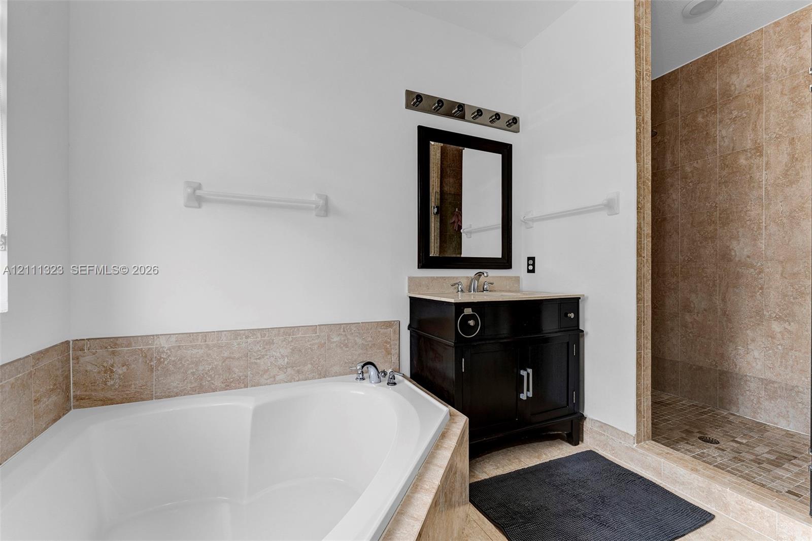 Corner soaking tub with stone surround, dark finish vanity featuring a stone countertop, and a walk-in shower with tiled walls