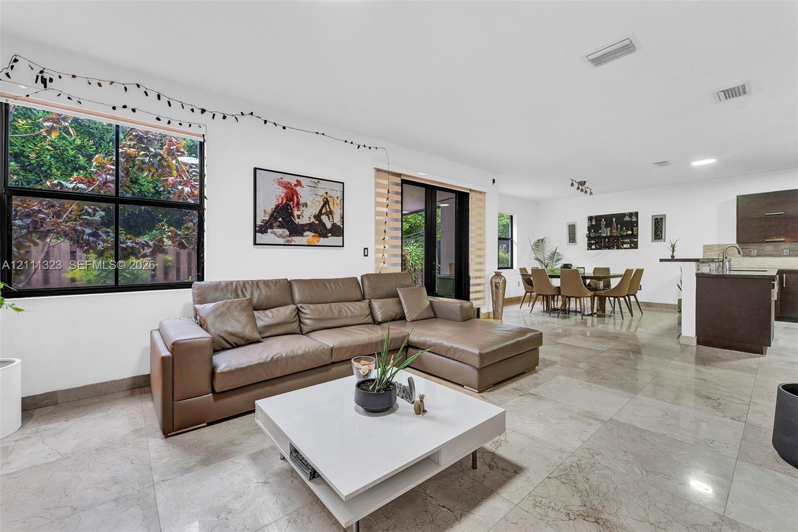Large-format stone tile flooring, expansive windows with black frames, recessed lighting, and a kitchen peninsula with dark cabinetry