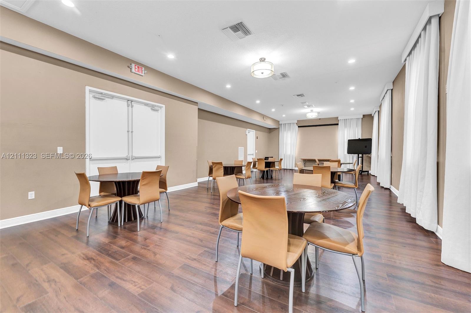 Spacious multipurpose room featuring wood-finish flooring, recessed lighting, neutral wall paint, and floor-to-ceiling drapery