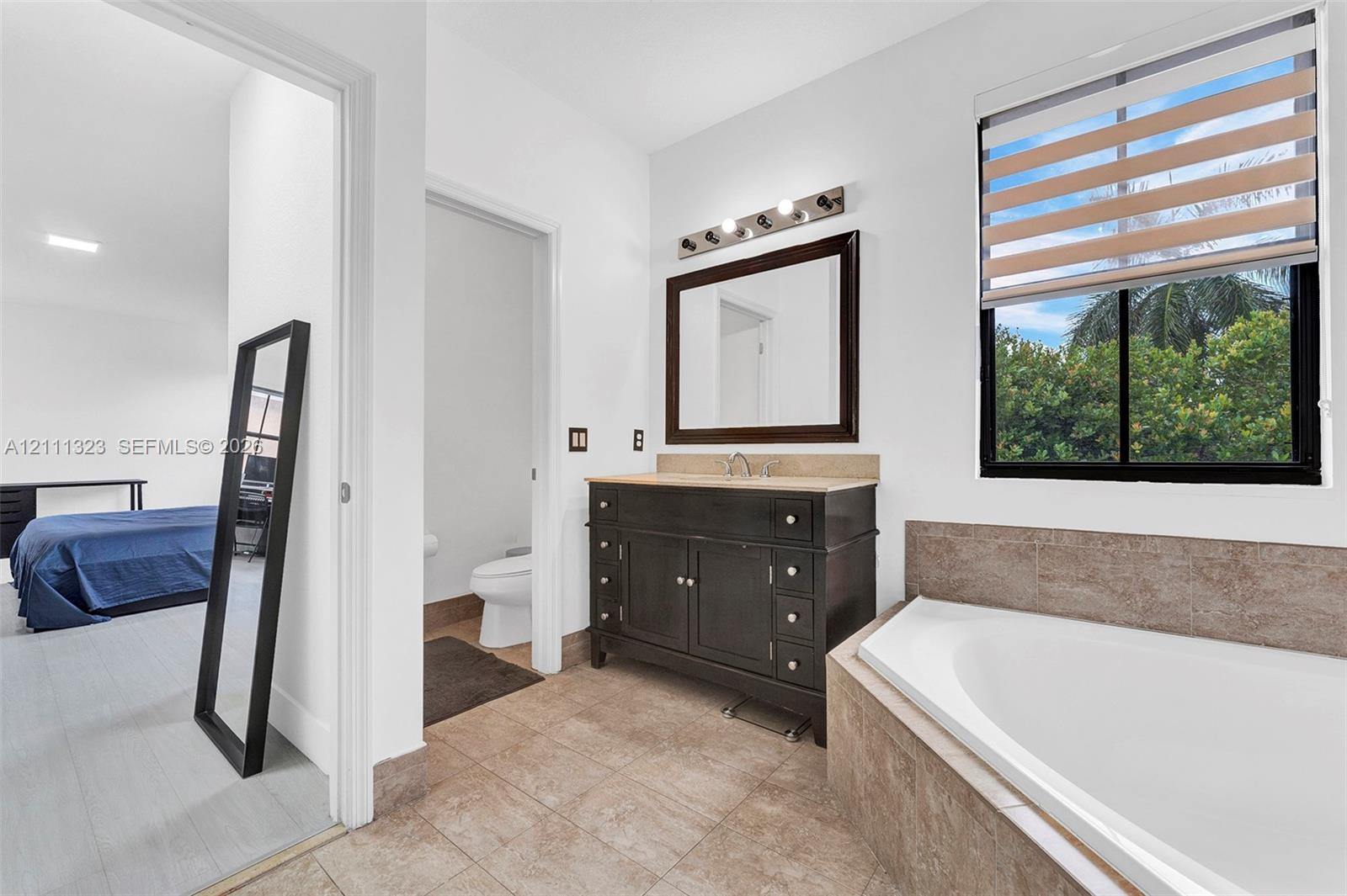 Bathroom featuring a vanity with dark cabinetry, stone-surfaced countertop, built-in soaking tub, multi-light fixture, and ceramic tile flooring