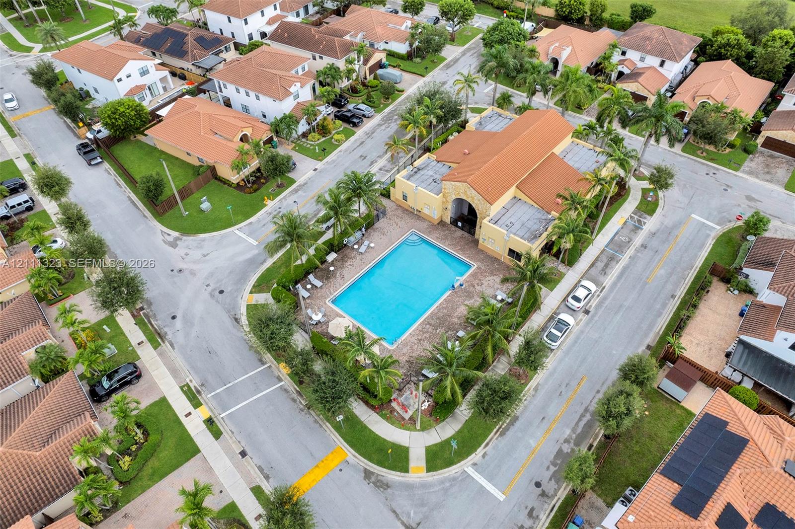 Community clubhouse featuring a tile roof, an outdoor swimming pool, a surrounding brick-paver deck, and mature palm landscaping