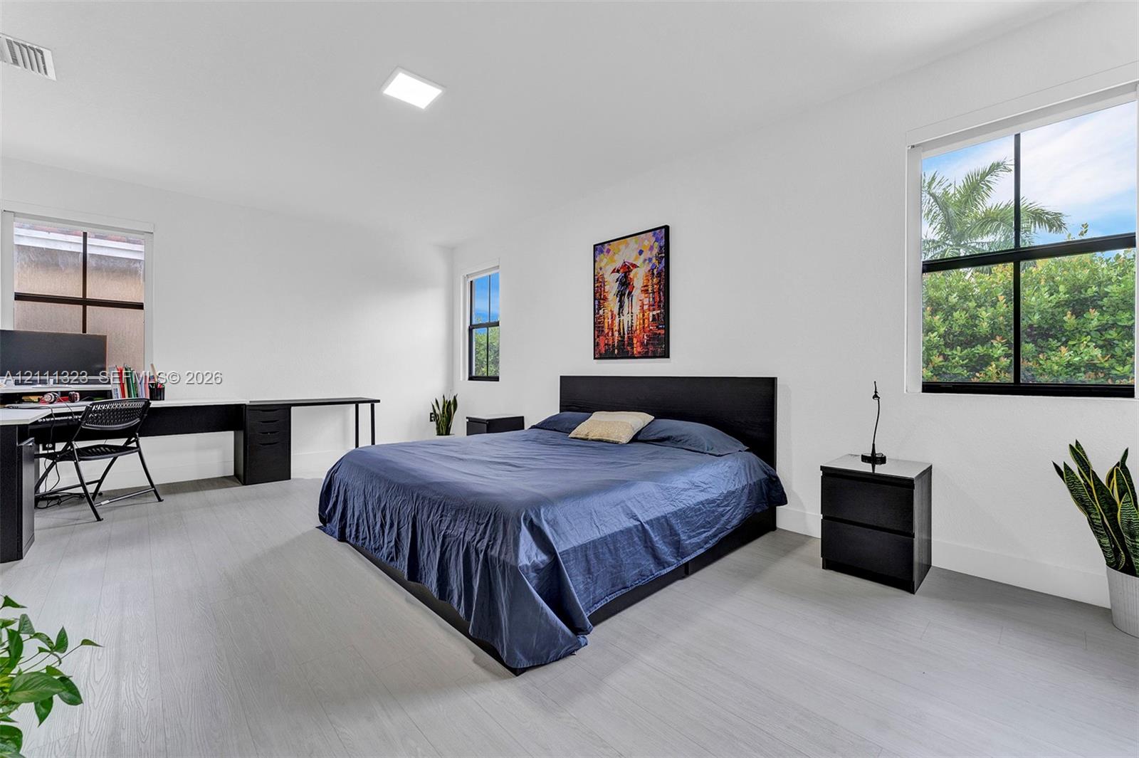 Spacious room featuring neutral walls, light wood-finish flooring, recessed lighting, and multiple windows with black trim