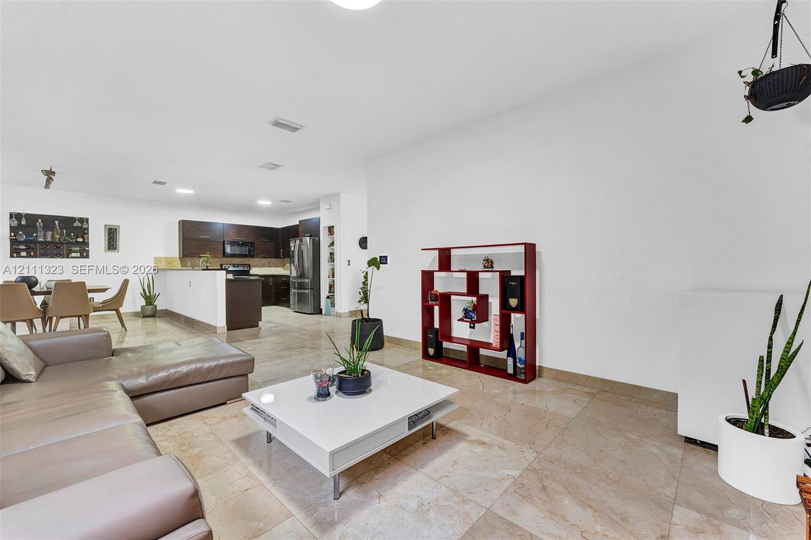 Open-concept interior featuring large-format tile flooring, recessed lighting, and a kitchen equipped with dark wood-finish cabinetry, stainless steel appliances, and a peninsula counter