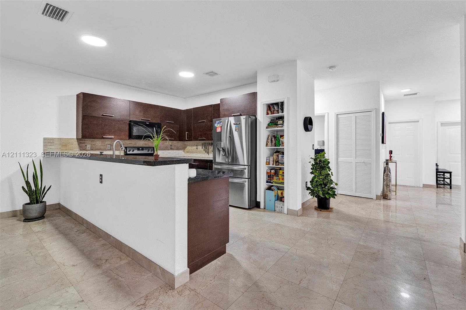 Kitchen featuring dark wood-finish cabinetry, stone countertops, stainless steel appliances, a built-in pantry, and large-format tile flooring