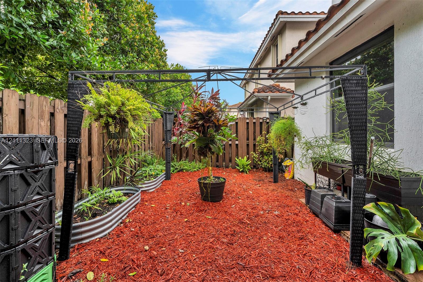 Private backyard featuring wood privacy fencing, galvanized steel raised garden beds, and red mulch ground cover
