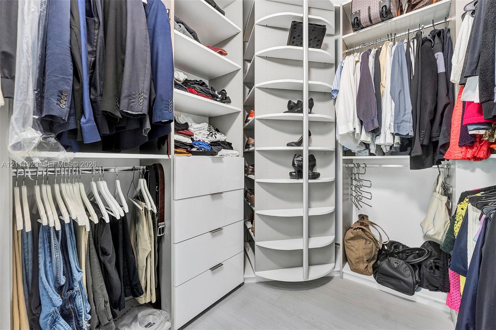 Custom walk-in closet featuring white built-in cabinetry, floor-to-ceiling adjustable shelving, integrated drawer storage, and a rotating shoe organizer