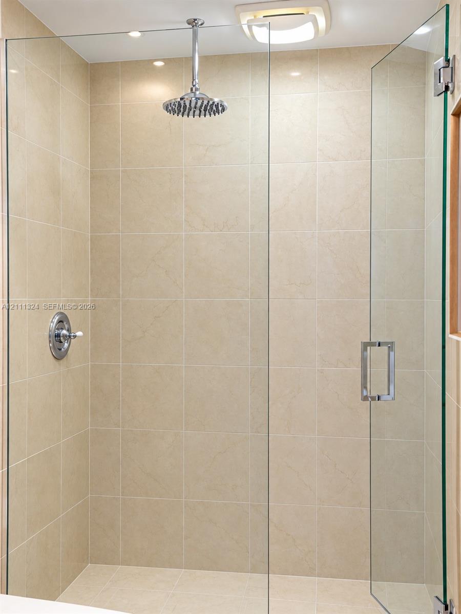Walk-in shower featuring floor-to-ceiling tile, frameless glass enclosure, polished chrome rainfall showerhead, and a matching temperature control valve