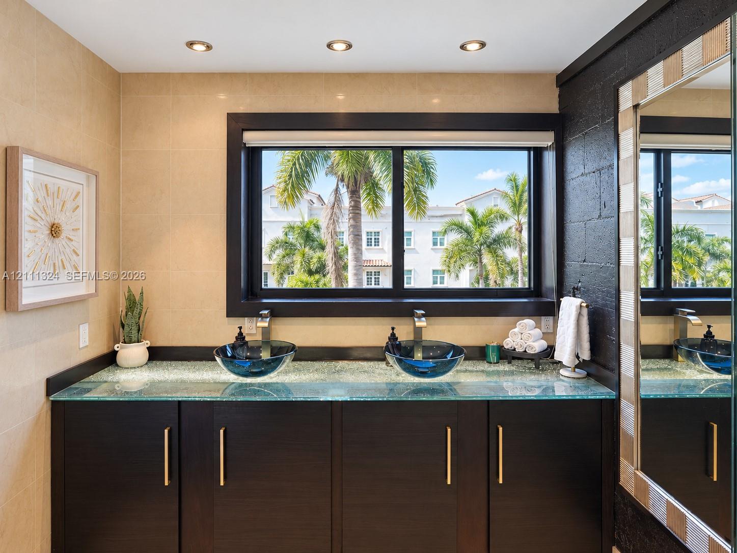 Dual vanity featuring a glass countertop, dark espresso-finish cabinetry, metallic hardware, and two blue glass vessel sinks with modern chrome faucets