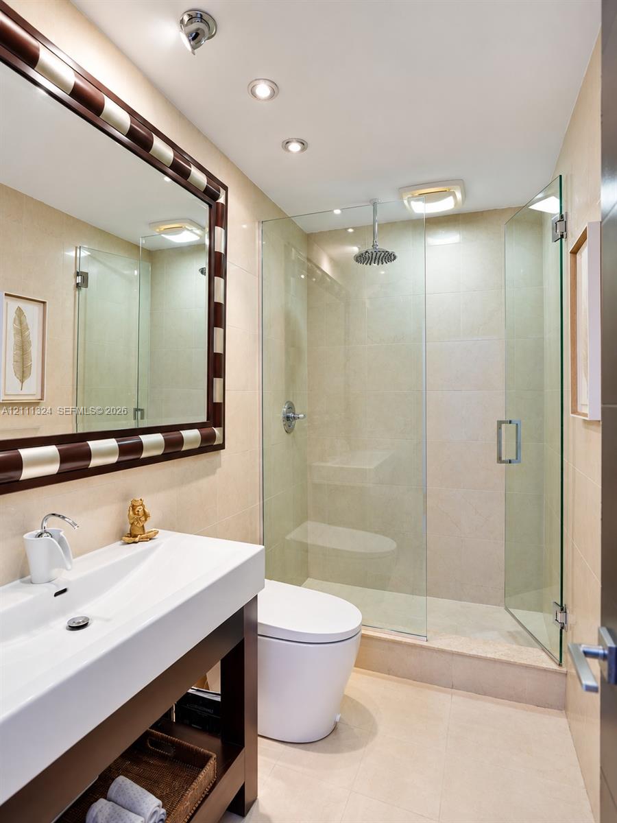 Bathroom featuring a floating vanity with a rectangular sink, walk-in shower with a glass enclosure and rain-style showerhead, recessed lighting, and large-format tile wall cladding