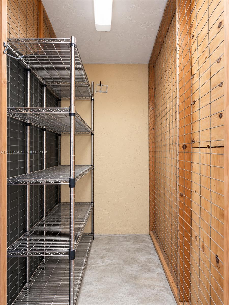 Storage space featuring metal wire shelving, plywood-paneled walls with wire grid overlays, and concrete flooring