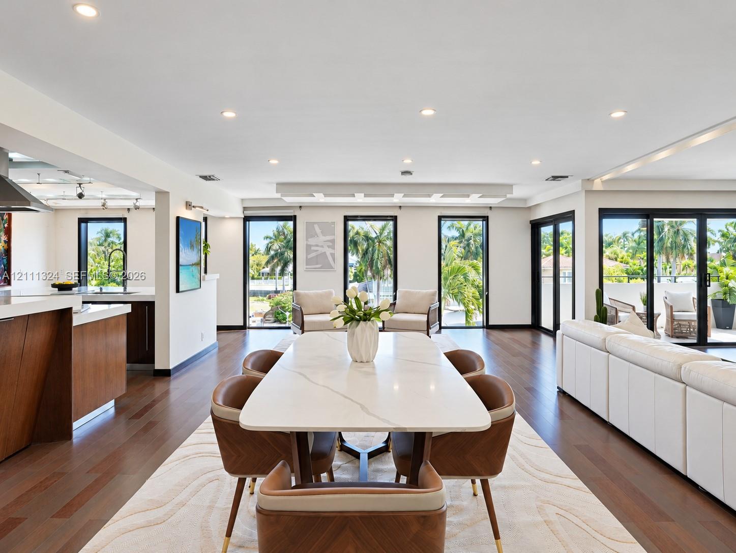 Open-concept interior featuring wood-finish flooring, recessed lighting, expansive glass sliding doors, and a built-in kitchen peninsula with a stone-finish countertop