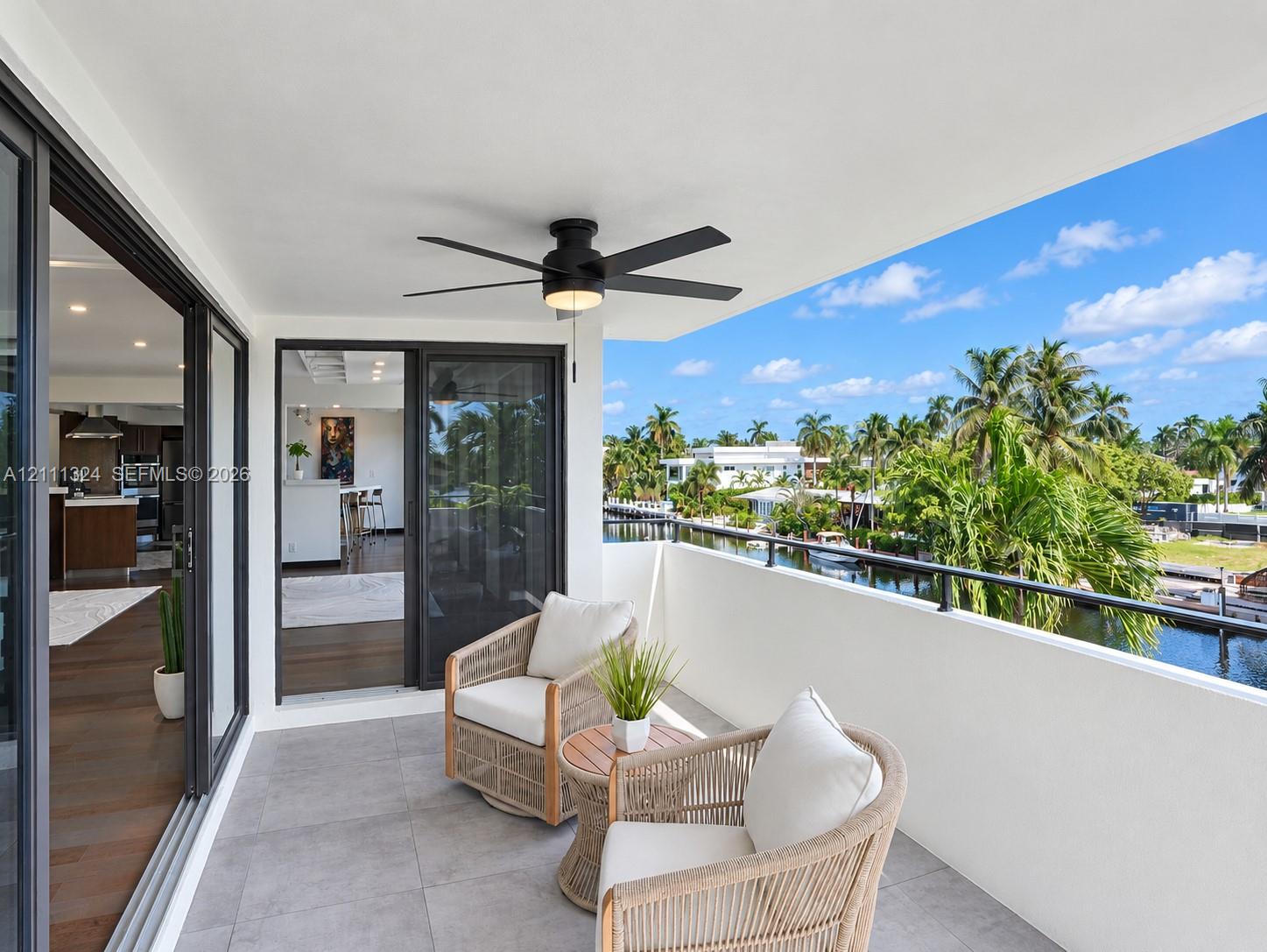 Covered terrace featuring large-format tile flooring, a matte black ceiling fan with integrated lighting, and a black metal railing overlooking the waterway