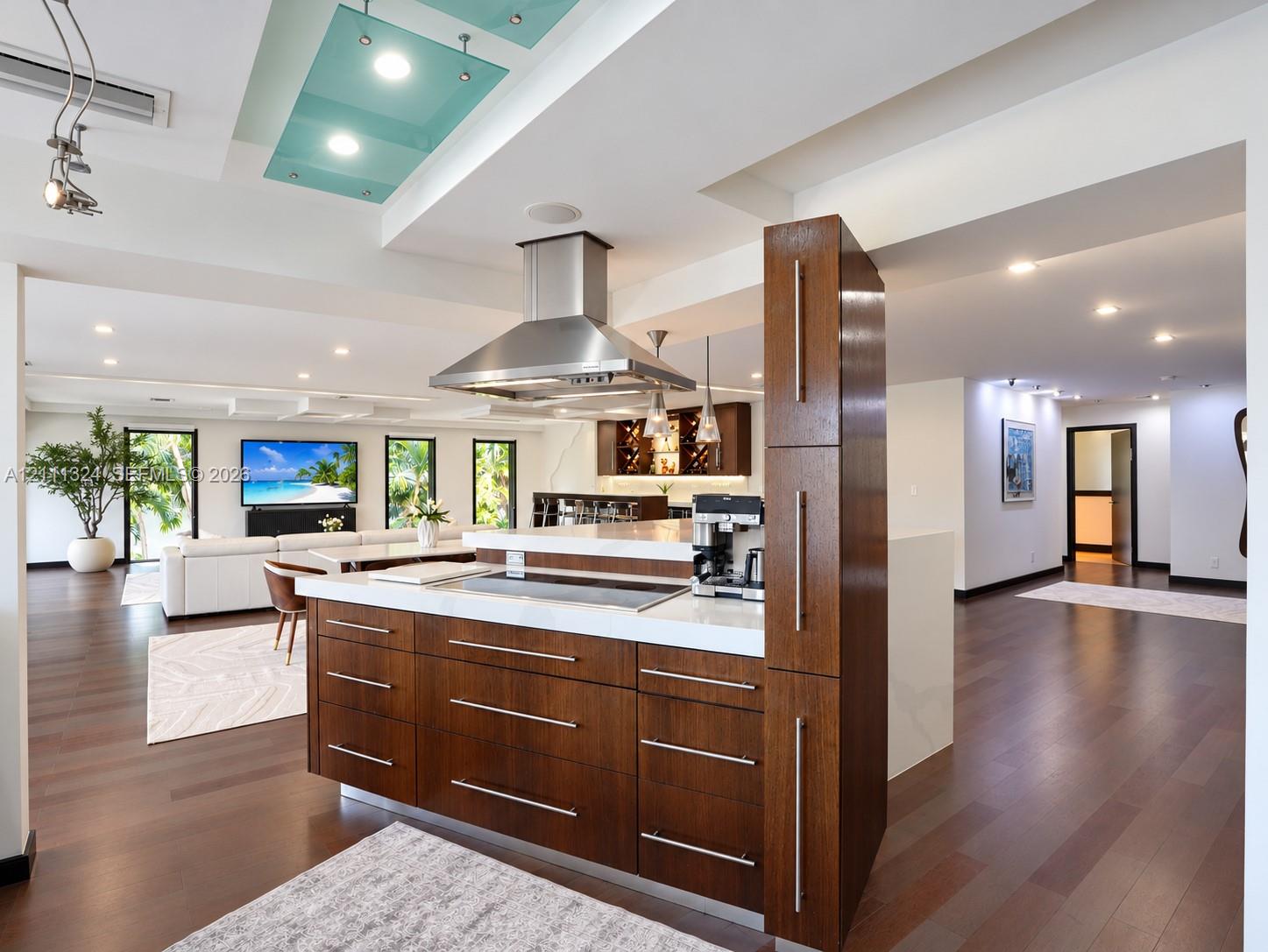 Kitchen island with dark wood-finish cabinetry, solid surface countertop, stainless steel cooktop, and stainless steel chimney range hood