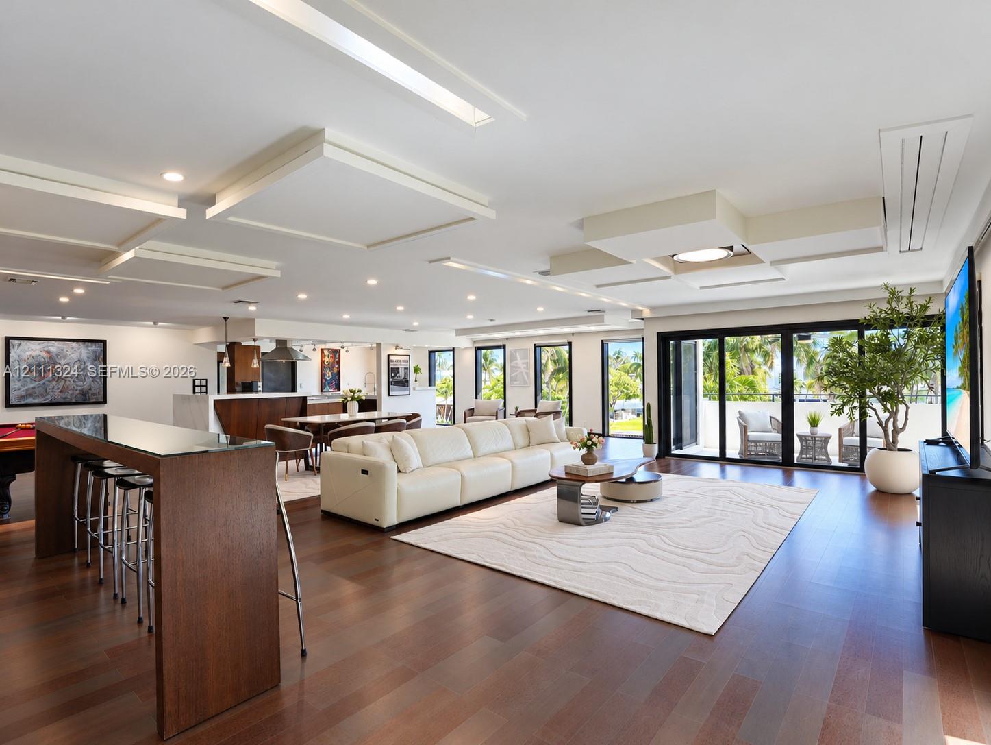 Open-concept interior featuring wood-finish flooring, custom geometric drop-ceiling detailing, recessed lighting, and expansive multi-panel sliding glass doors