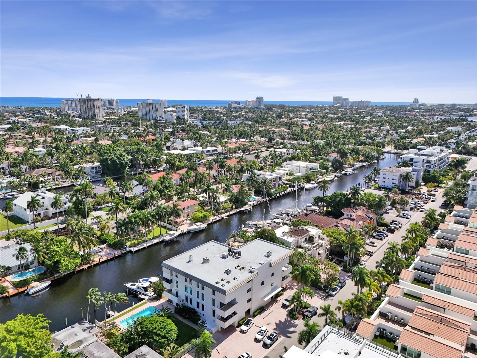 Aerial perspective of a multi-story residential building featuring a swimming pool, paved surface parking, and direct canal access
