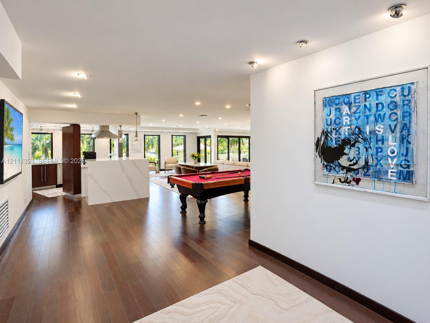 Open-concept space featuring wood-finish flooring, recessed lighting, and a kitchen island with a stone-surfaced countertop