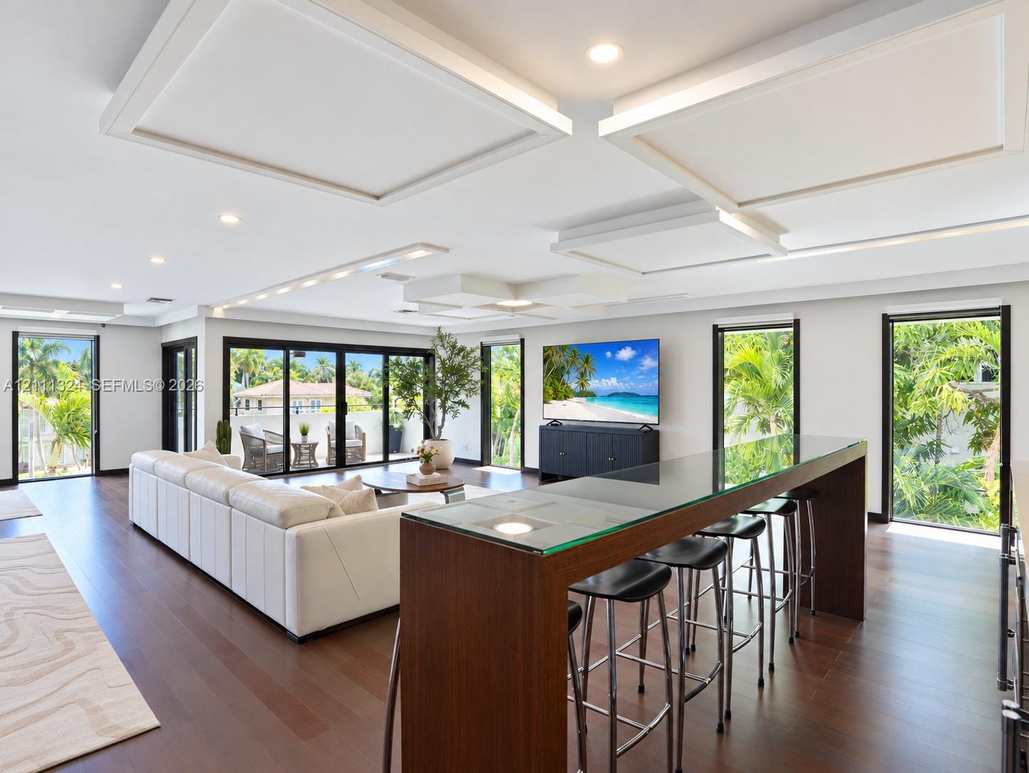 Coffered ceiling detailing, wood-finish flooring, recessed lighting, glass-topped breakfast bar, and multi-panel glass sliding doors