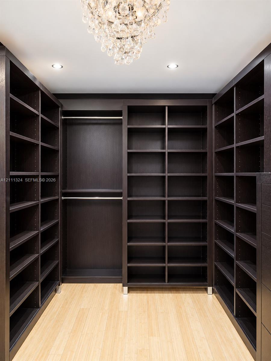 Custom dark-finish built-in shelving, wood-finish flooring, integrated metal hanging rods, and a tiered crystal chandelier