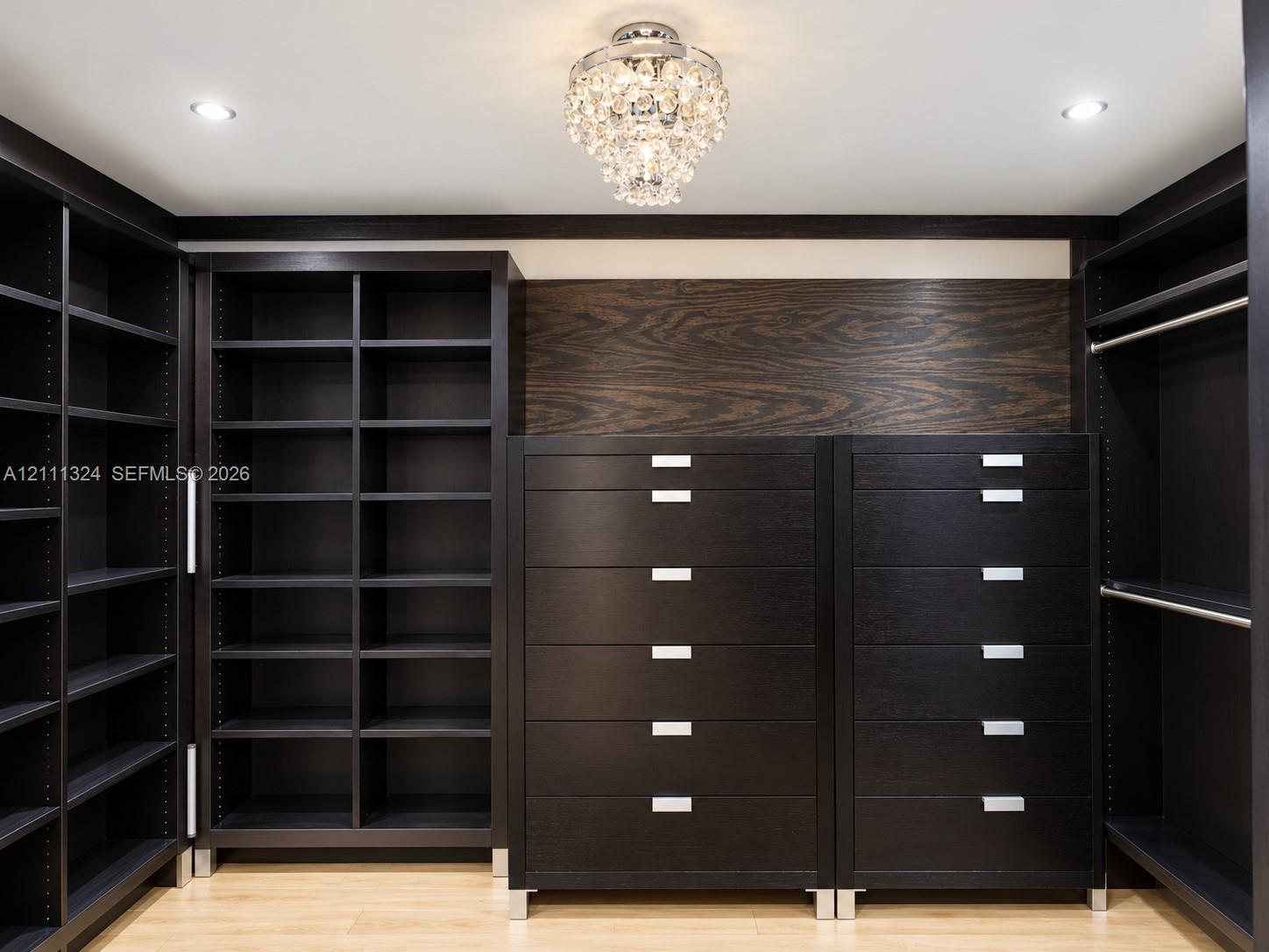 Custom dark wood-finish built-in cabinetry featuring extensive shelving, integrated drawer units with metallic hardware, and a center decorative crystal chandelier