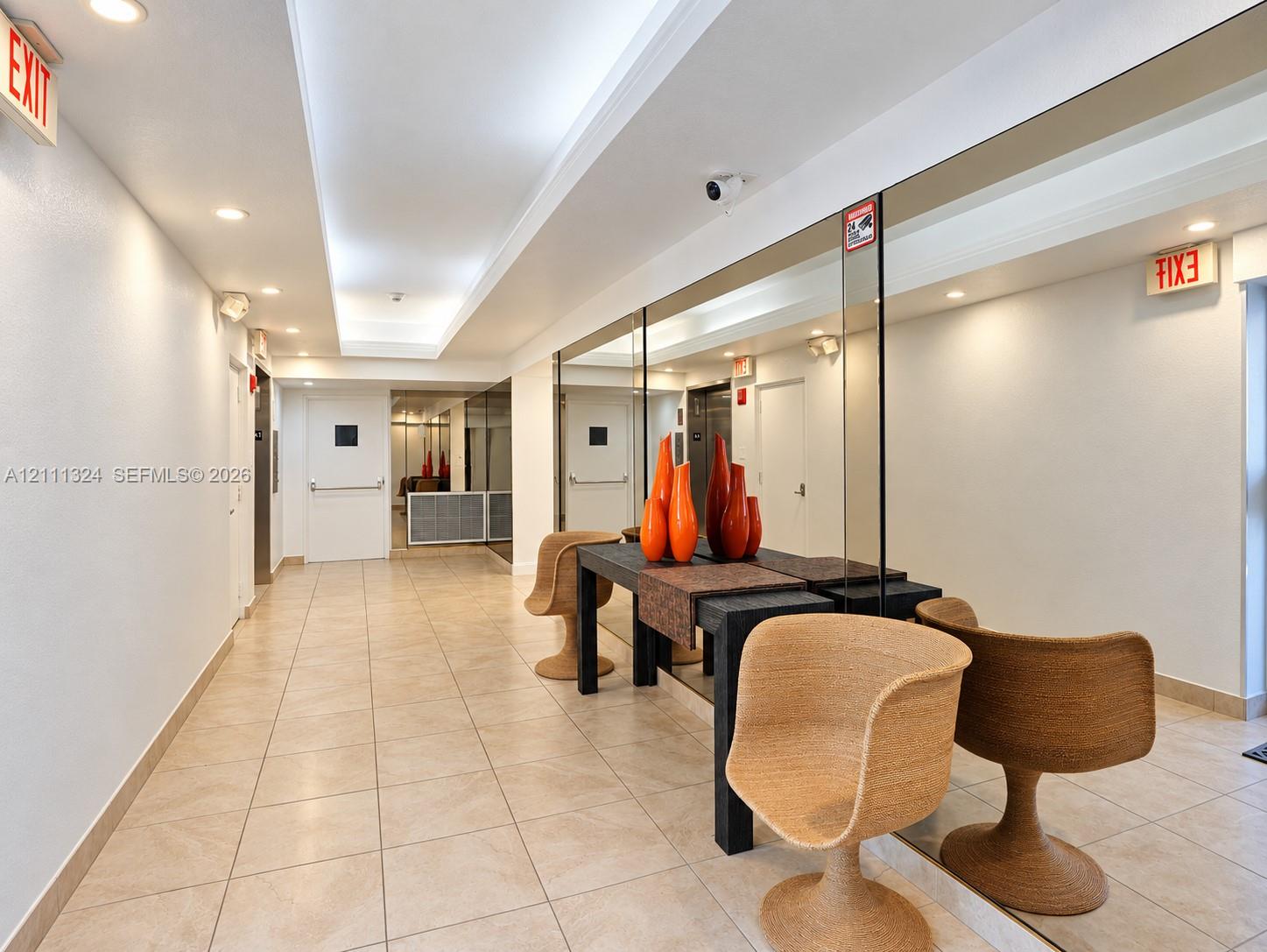 Hallway featuring tile flooring, recessed ceiling lighting, a tray ceiling detail, and floor-to-ceiling wall mirrors