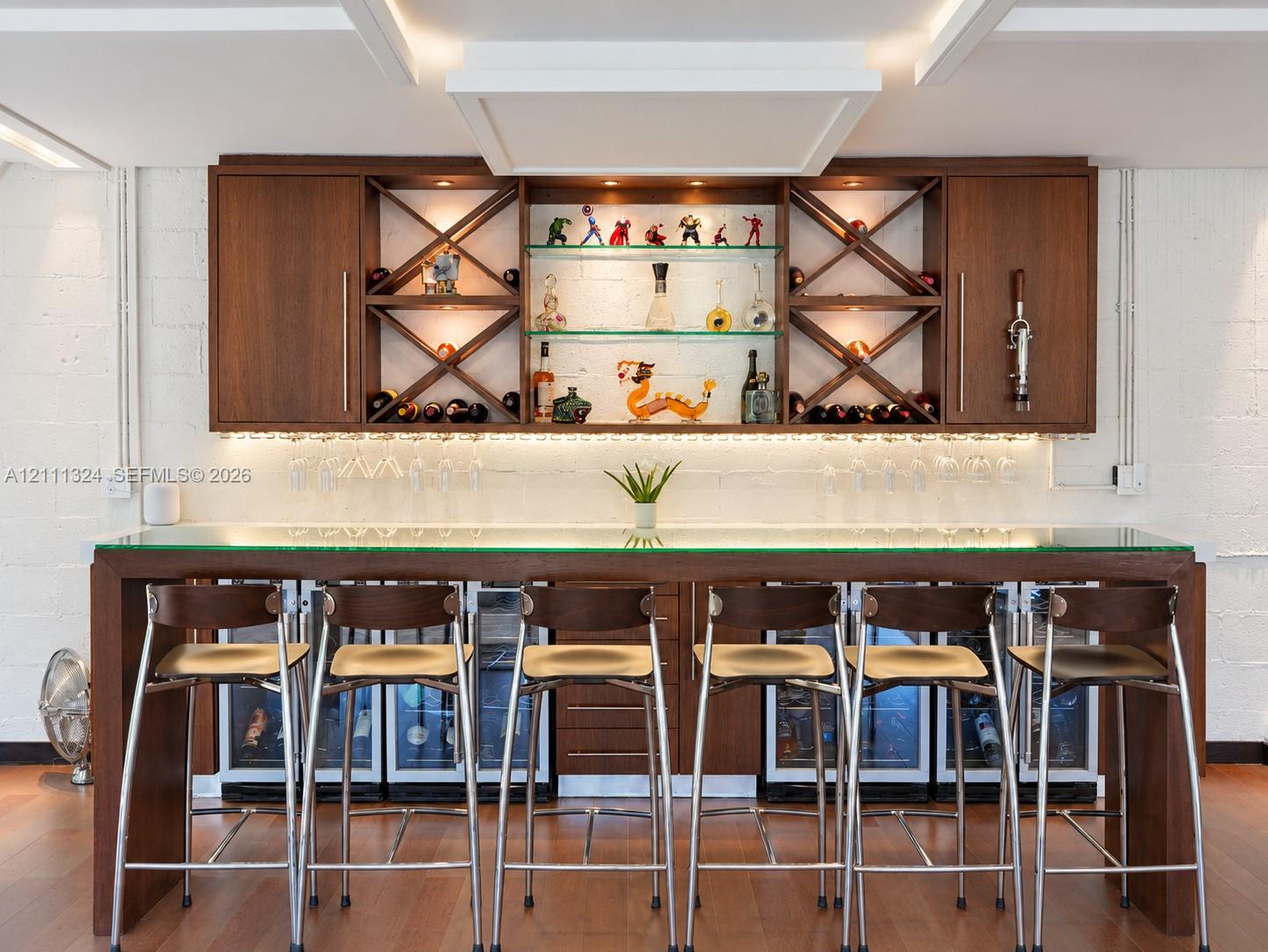 Custom built-in bar featuring wood cabinetry, integrated glass shelving with X-frame detailing, under-cabinet lighting, and a glass-top counter with multiple under-counter refrigeration units