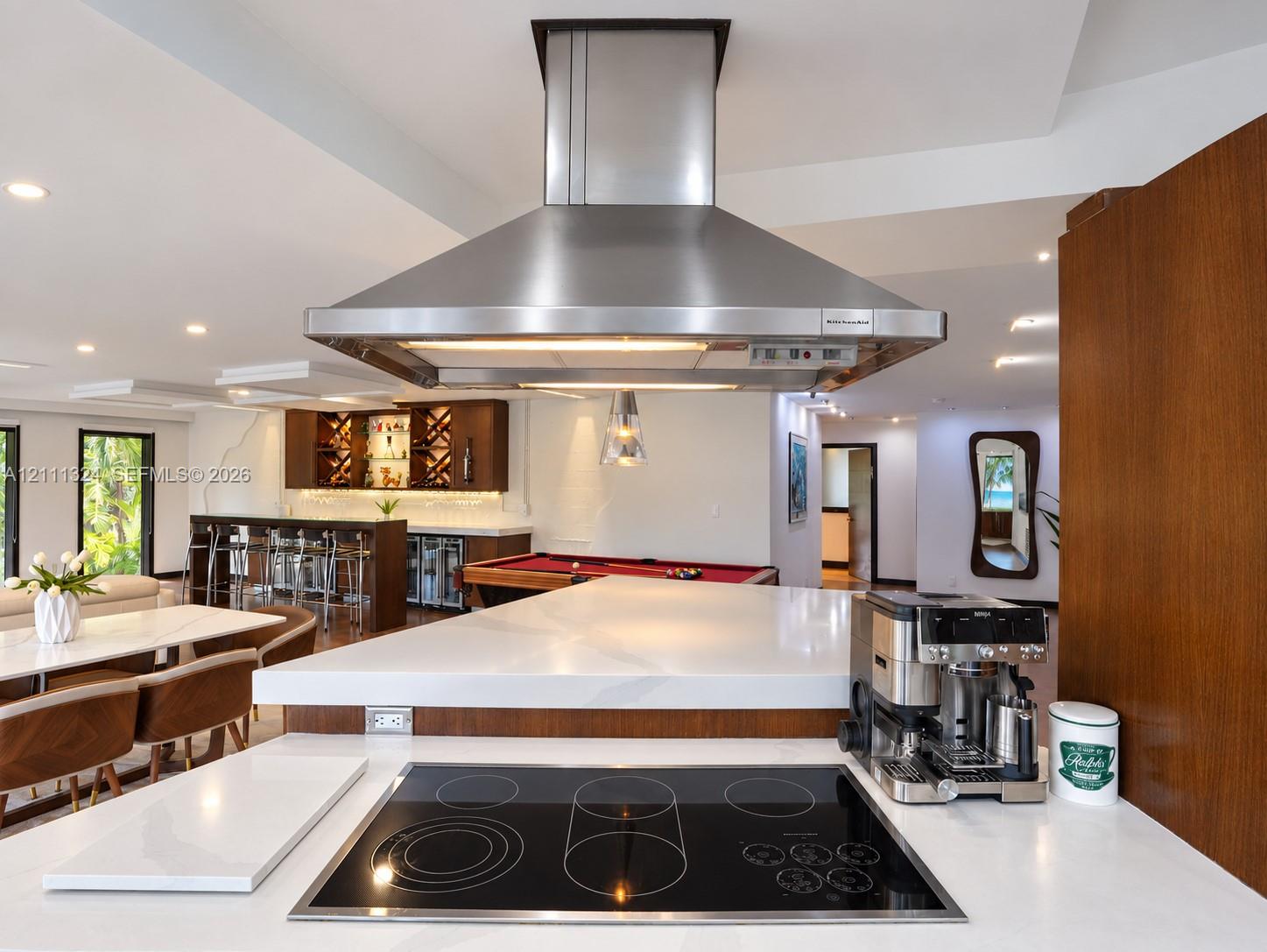 Kitchen featuring a white solid-surface countertop with an integrated electric cooktop, a stainless steel chimney-style range hood, and wood-finish cabinetry