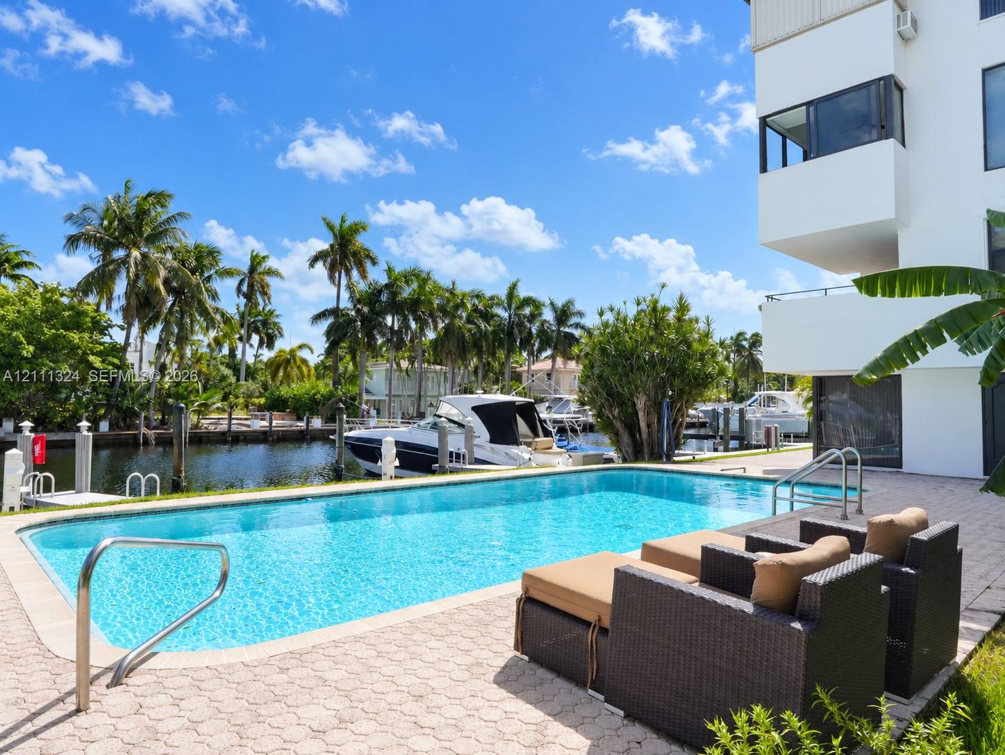 Waterfront swimming pool with paver decking, metal handrails, and direct bulkhead access to a canal