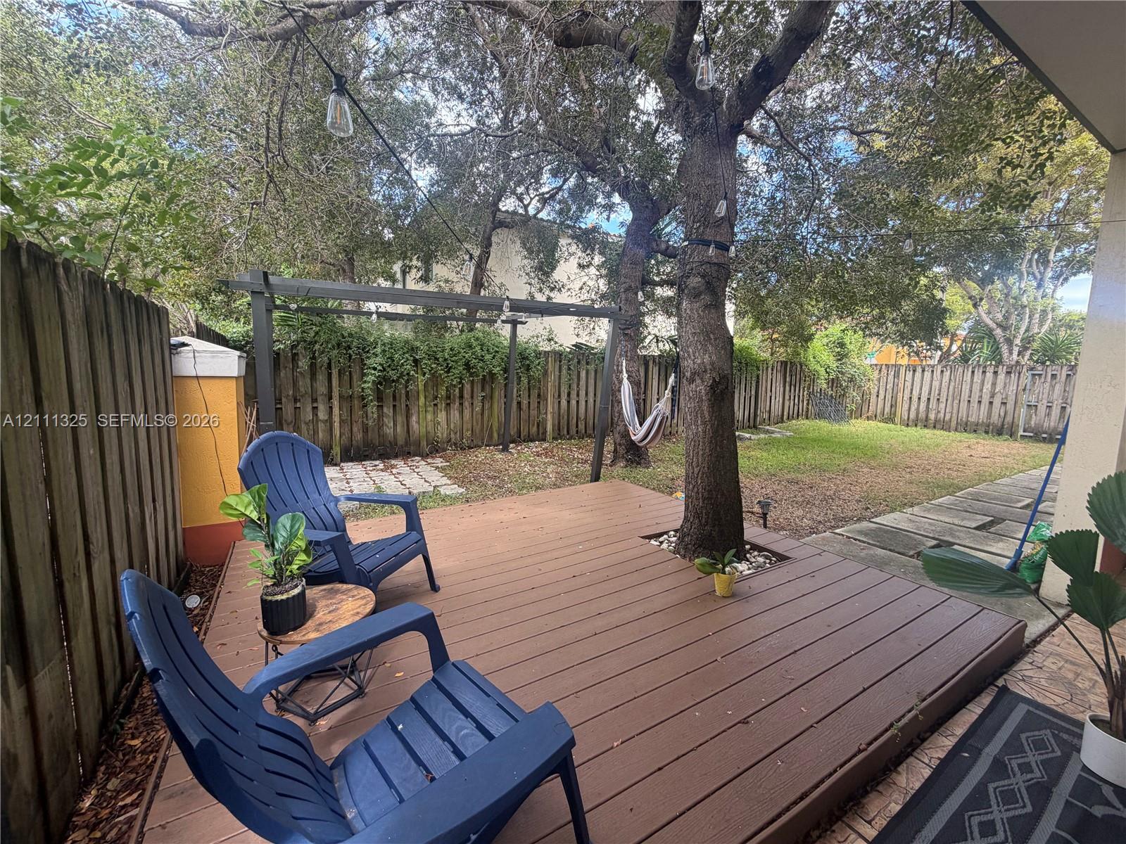 Backyard featuring a wood-finish deck, mature trees, a metal pergola, and a privacy fence