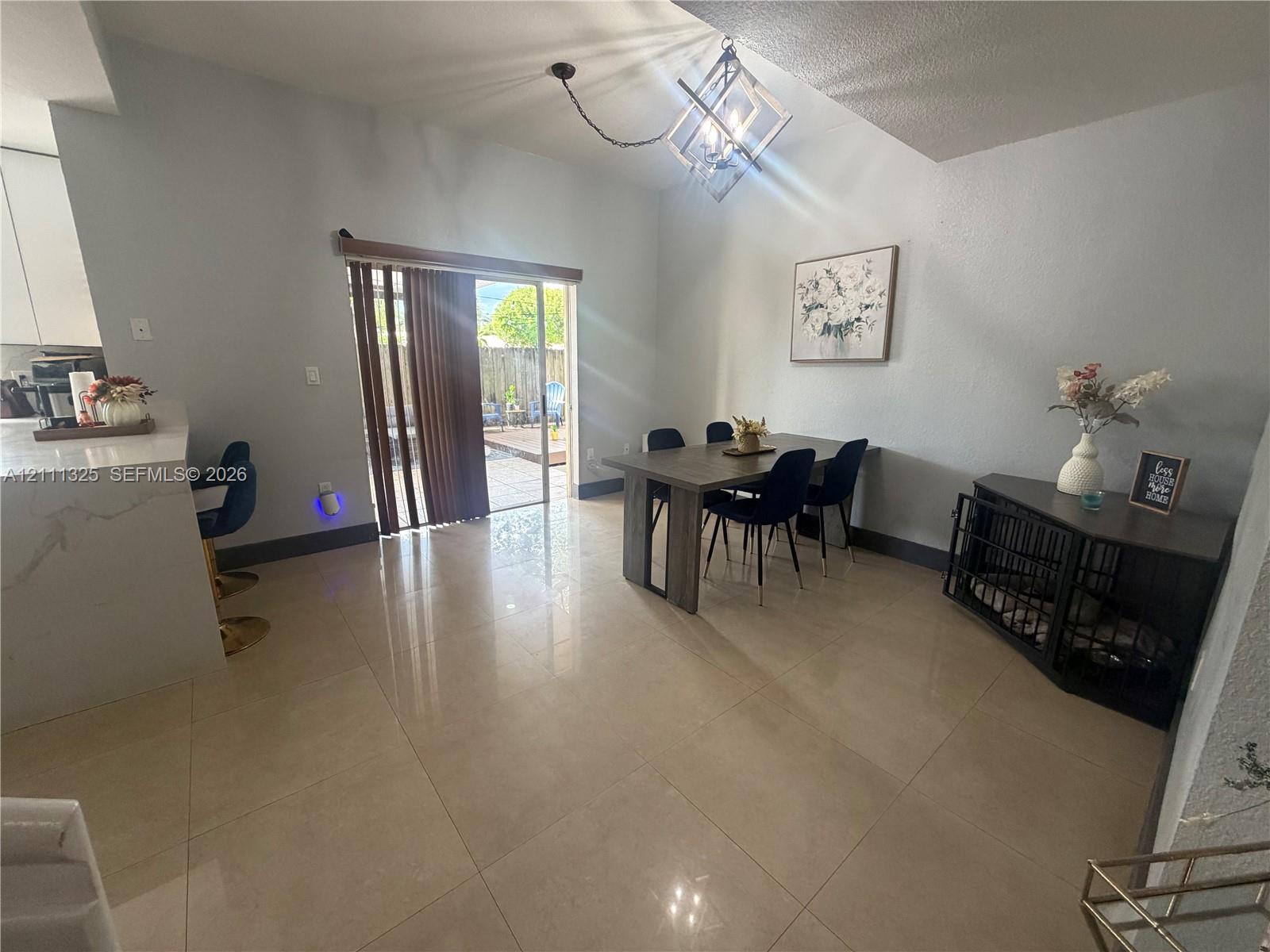 Large-format tile flooring, vaulted ceiling with geometric metal chandelier, and sliding glass patio door