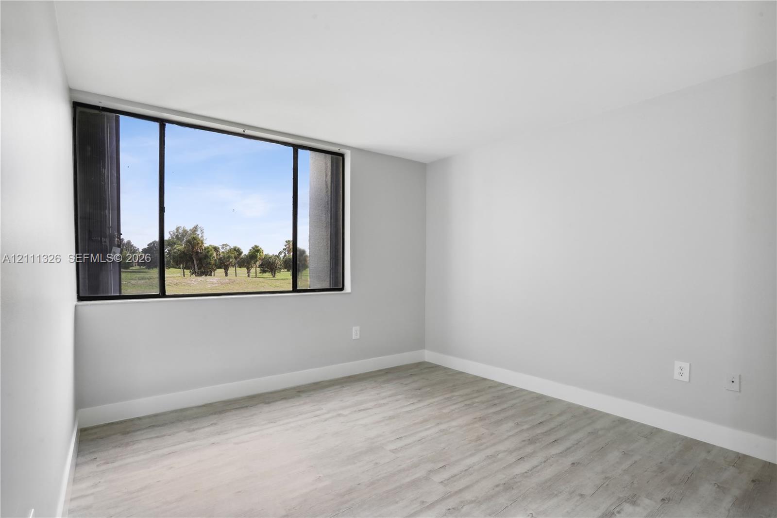 Primary bedroom featuring neutral-toned walls, laminate wood-look flooring, and a large horizontal window with a landscape backdrop.