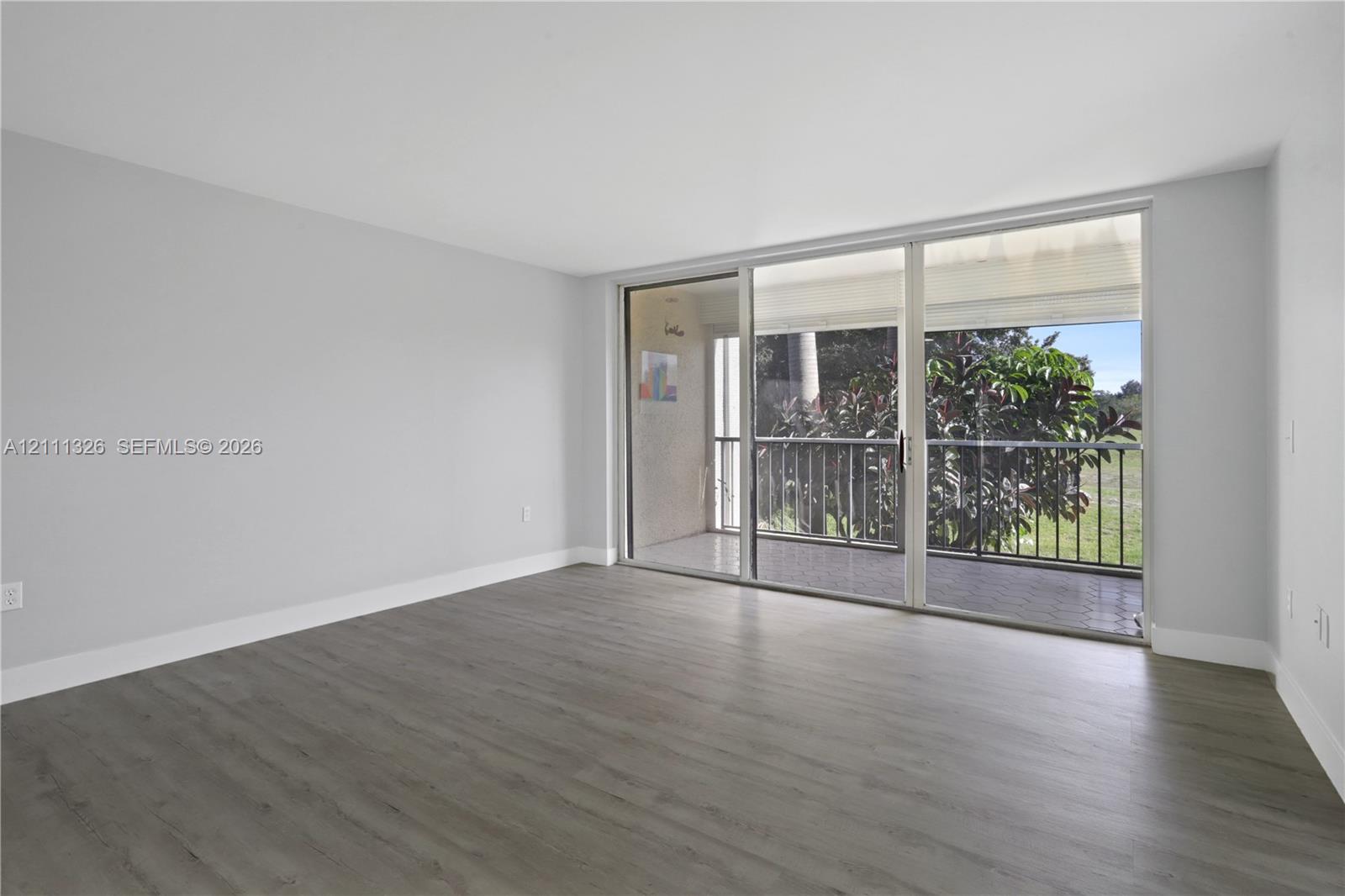 Living area featuring wood-look laminate flooring, crisp white walls, and expansive floor-to-ceiling sliding glass doors opening to a private screened-in balcony.