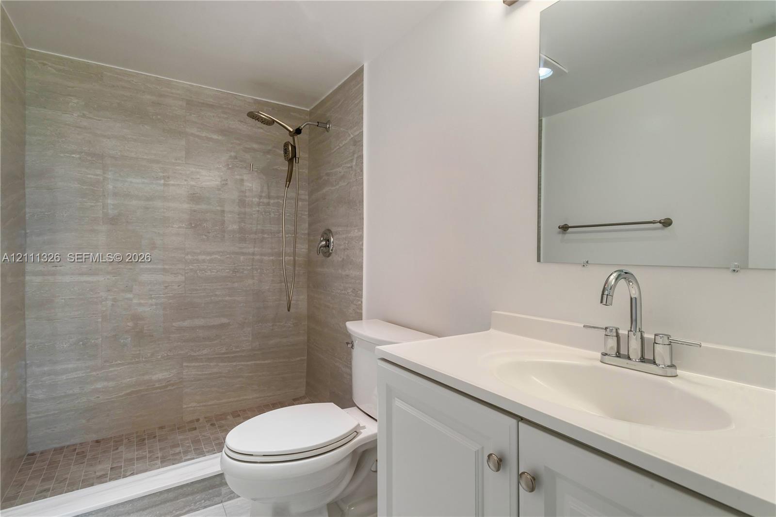 Walk-in shower with tile surround, white vanity with integrated sink, and wall-mounted mirror.