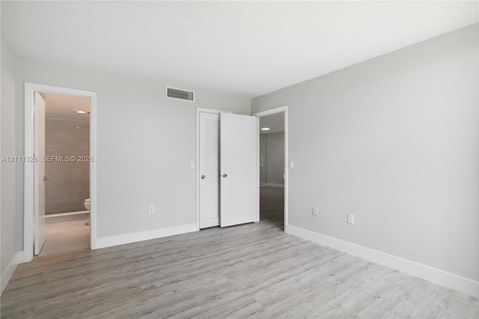 Primary bedroom featuring crisp white walls, laminate wood-look flooring, and a walk-in closet and en suite bathroom with a walk-in shower.